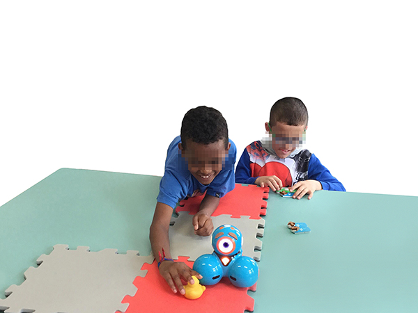 Two blind children playing with Dash (a small robot) on a foam carpet