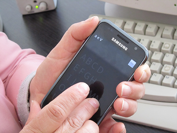 A user holding a smartphone and typing using an alternative keyboard.